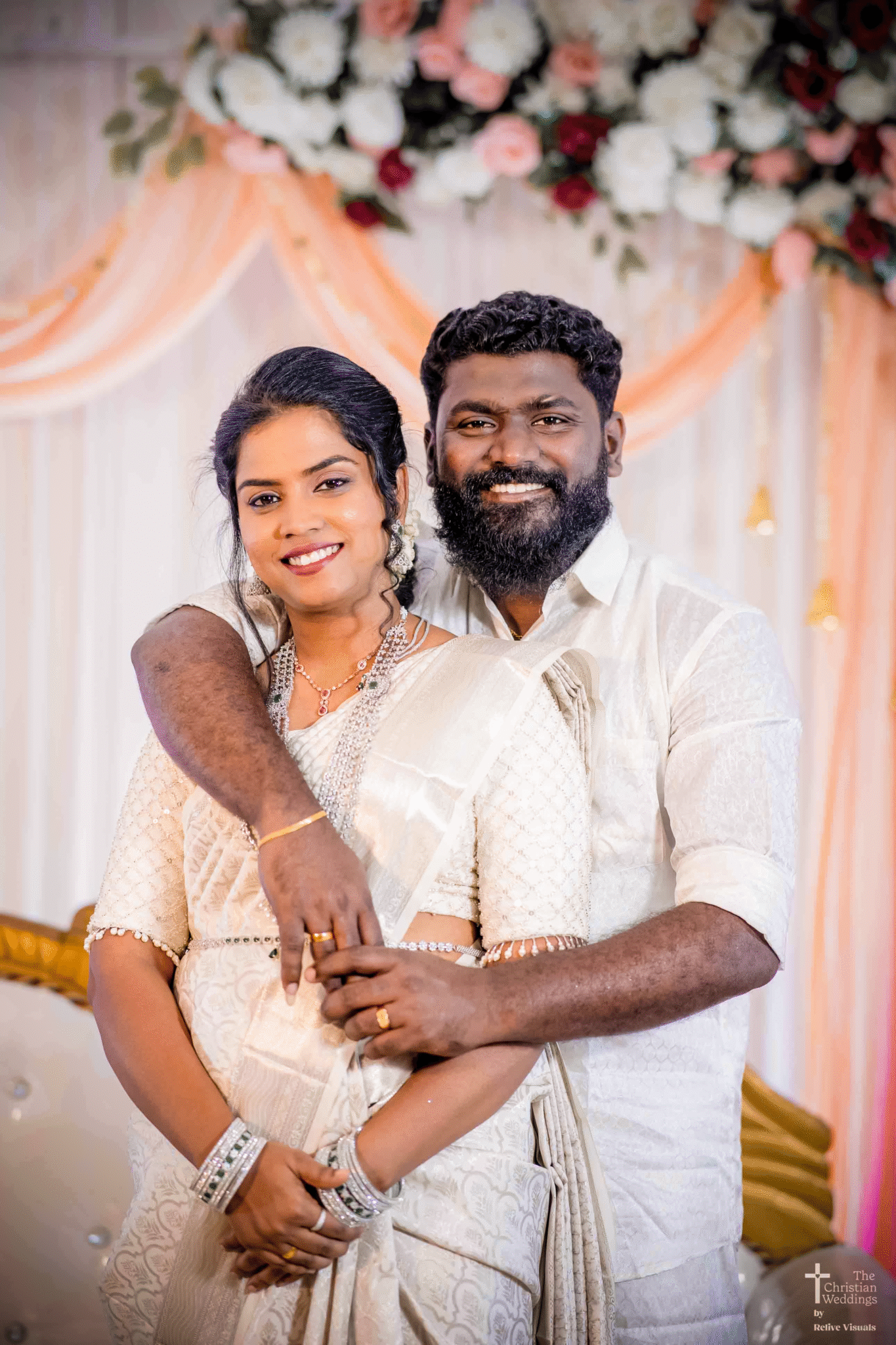 The groom lovingly wraps his arms around the bride from behind, their smiles radiating joy and affection on their engagement day.