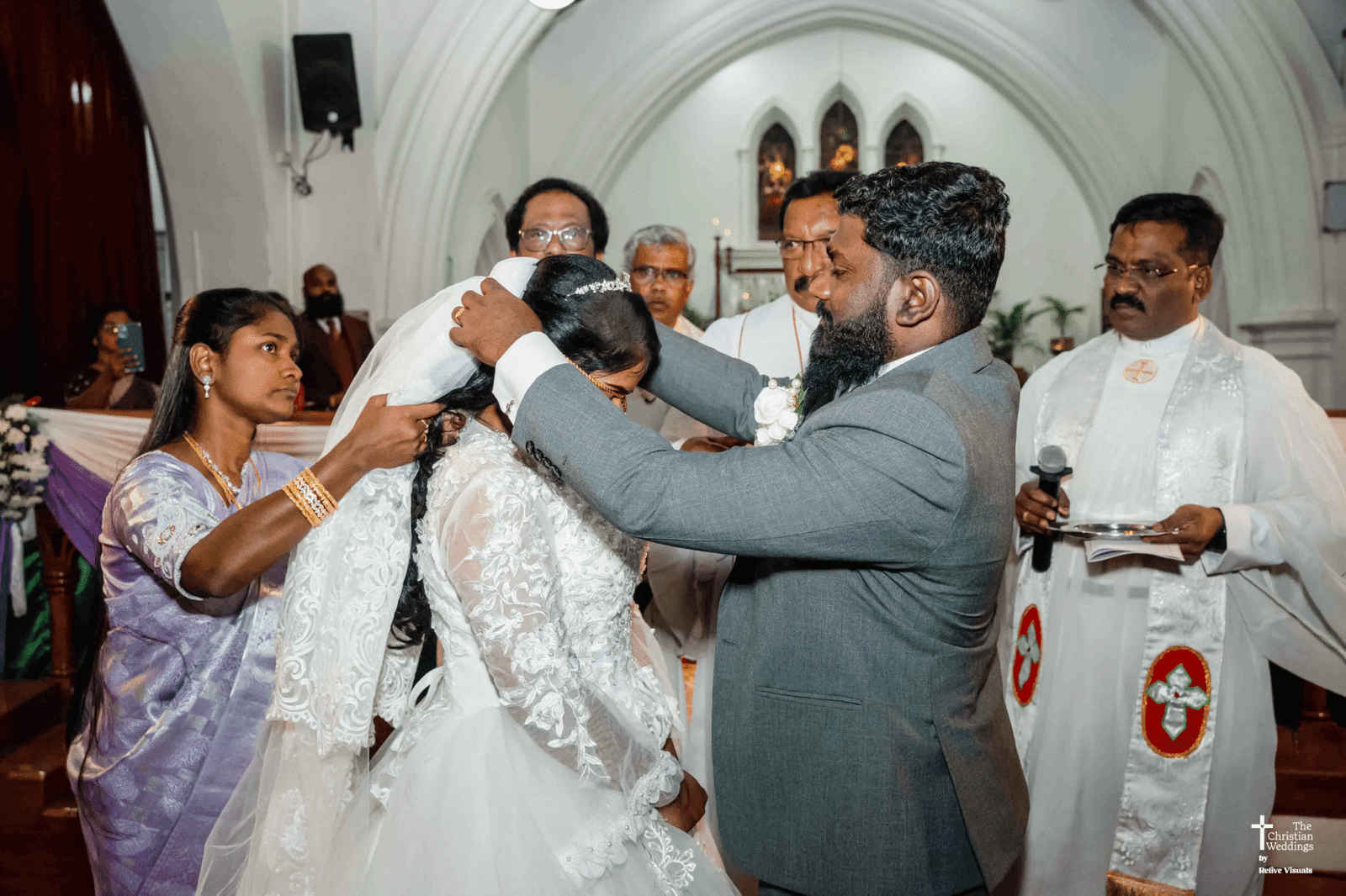 The groom gently places a traditional wedding chain around the bride’s neck during the ceremony, symbolizing their union.