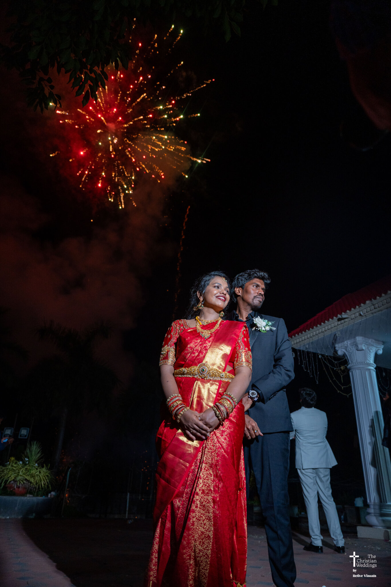 Bride and groom standing together with sparkling firecrackers lighting up the background during their wedding celebration.