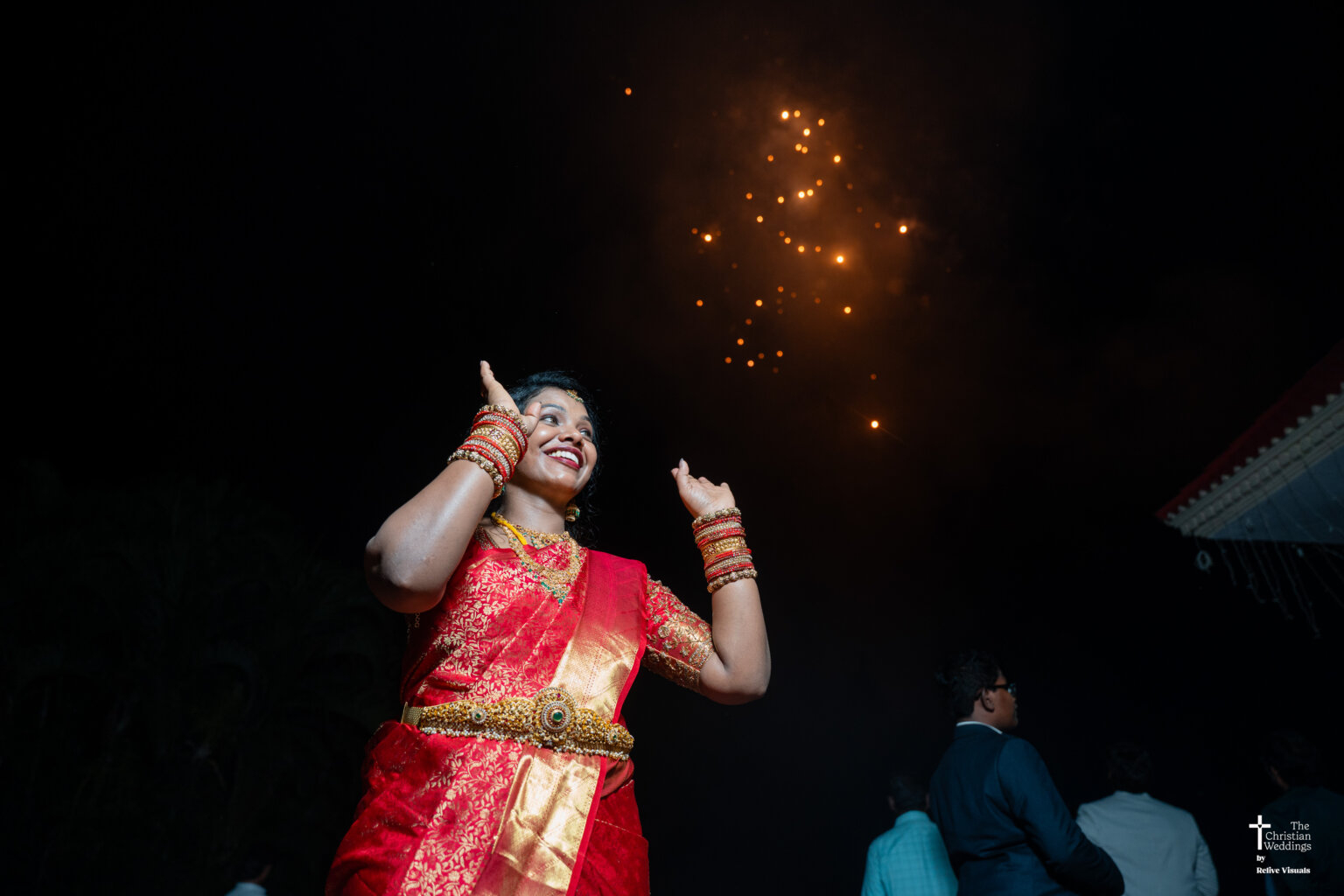 Christian bride looking up and smiling joyfully as colorful firecrackers burst in the sky during the celebration.