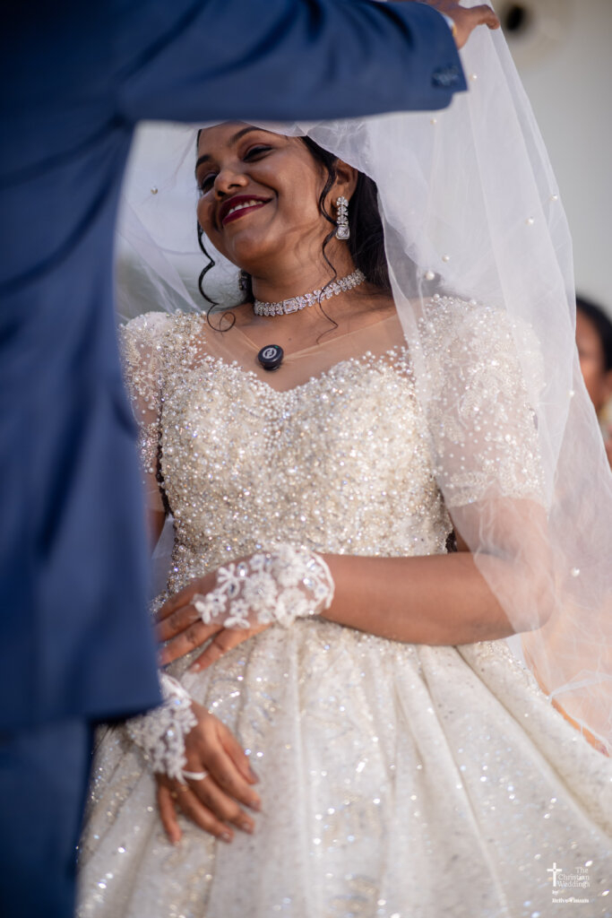 Christian groom gently removing the bride’s veil (veni) as she smiles warmly.