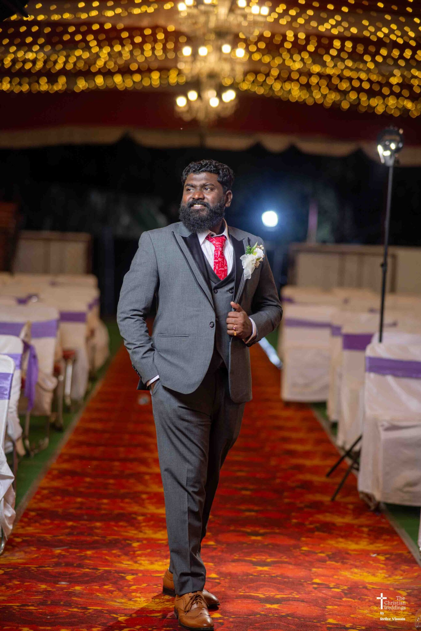 The groom stands confidently during the wedding reception, dressed sharply and smiling warmly as guests celebrate around him